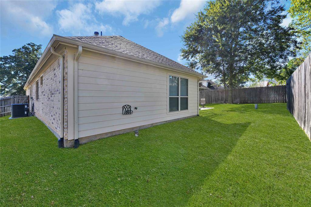 The photo shows a side view of a single-story home with light brick and siding. It features a well-maintained green lawn and a private fenced backyard, ideal for outdoor activities.