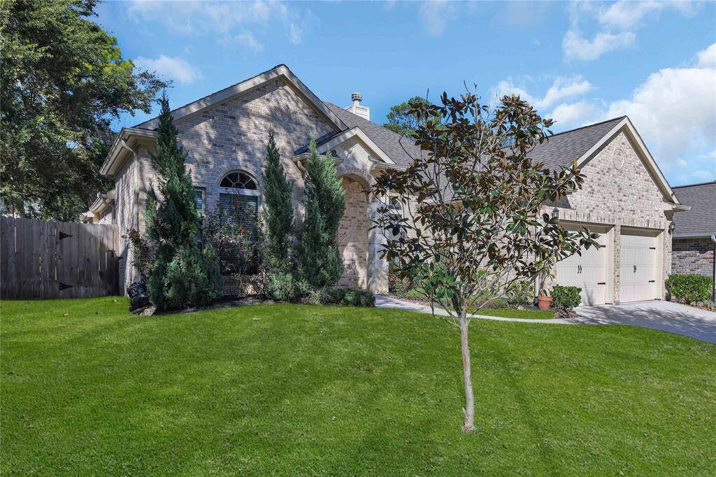 This charming home features a brick exterior with a well-maintained lawn and mature landscaping, including tall shrubs and a small tree. It has a two-car garage and a welcoming front entrance, offering great curb appeal in a serene neighborhood setting.