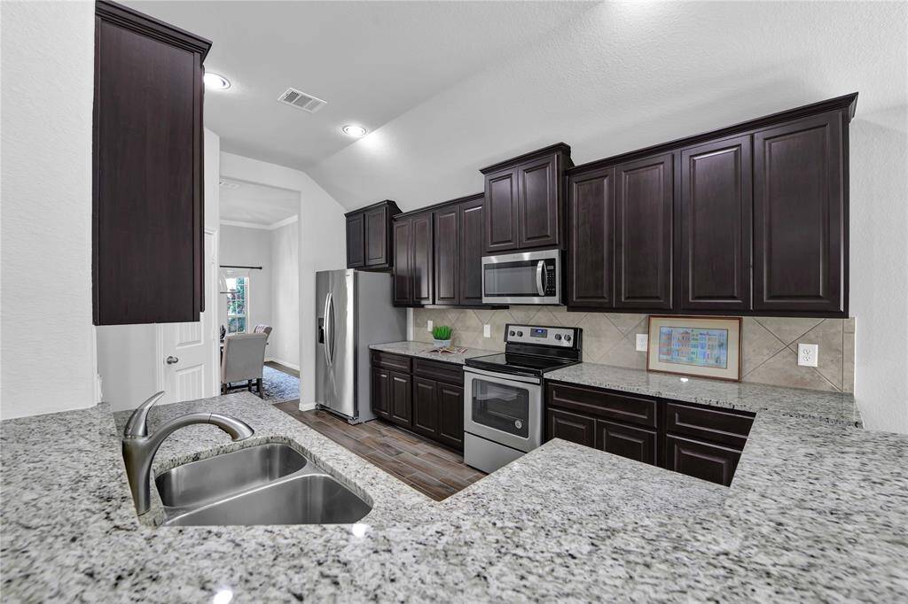 This photo showcases a modern kitchen featuring dark wood cabinets, granite countertops, and stainless steel appliances. The space is open and well-lit, with a view into an adjacent dining area.