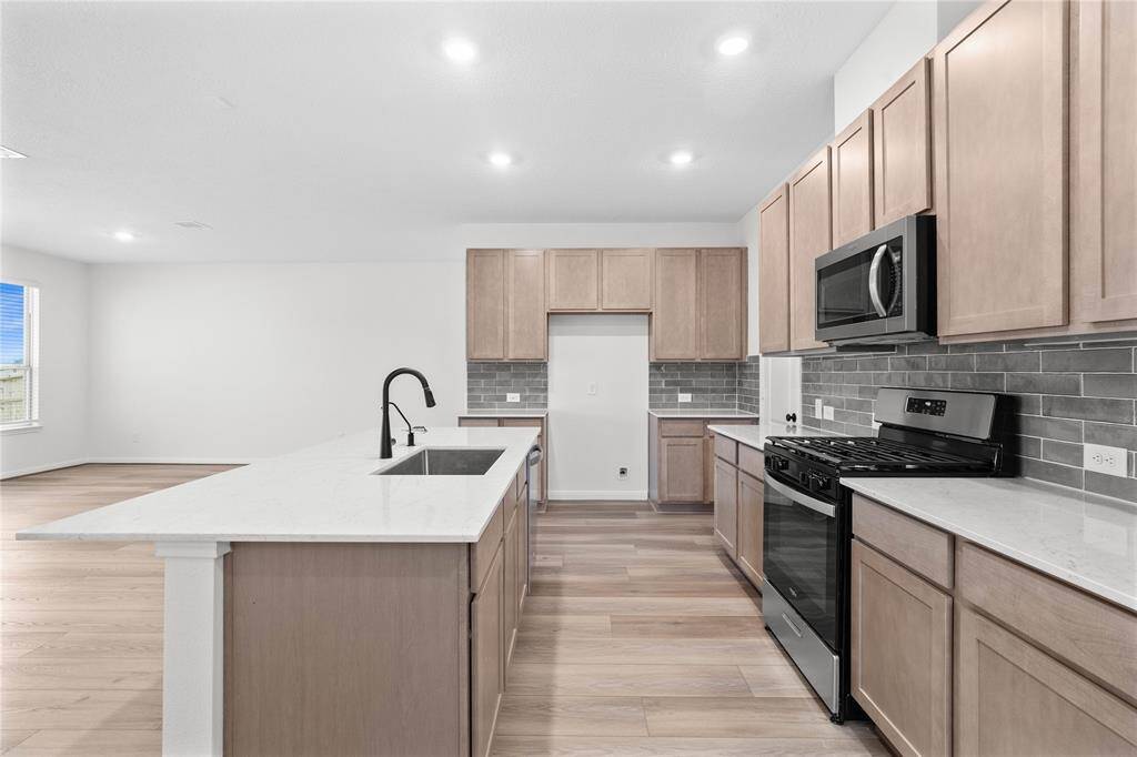 This spacious kitchen features high ceilings, stained wood cabinets, silestone countertops, SS appliances, modern tile backsplash, recessed lighting, large kitchen island with space for a breakfast bar, large windows with privacy blinds, and a pantry all overlooking your huge family room.