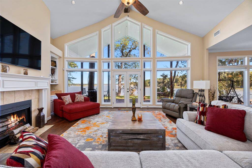 The family room boasts soaring high ceilings and expansive windows that frame breathtaking views of Lake Livingston, creating a light-filled, airy space. A cozy fireplace anchors the room, inviting warmth and relaxation while overlooking the serene waterfront.