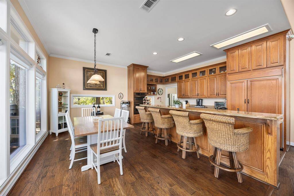 The kitchen is a chef’s dream, featuring custom cabinets, high-end appliances, and a built-in refrigerator for seamless style and function. The adjacent dining area is bathed in natural light, with floor-to-ceiling windows offering sweeping views of the waterfront and the boathouse, creating a perfect space for dining with a scenic backdrop.