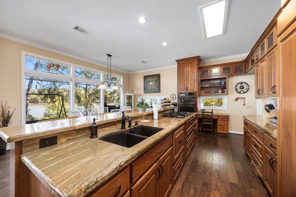 The kitchen features an expanded granite countertop with barstool seating, offering ample space for both meal prep and casual dining. Custom cabinets provide plenty of storage, while the built-in desk/work space adds convenience for managing tasks in this spacious and well-equipped kitchen.