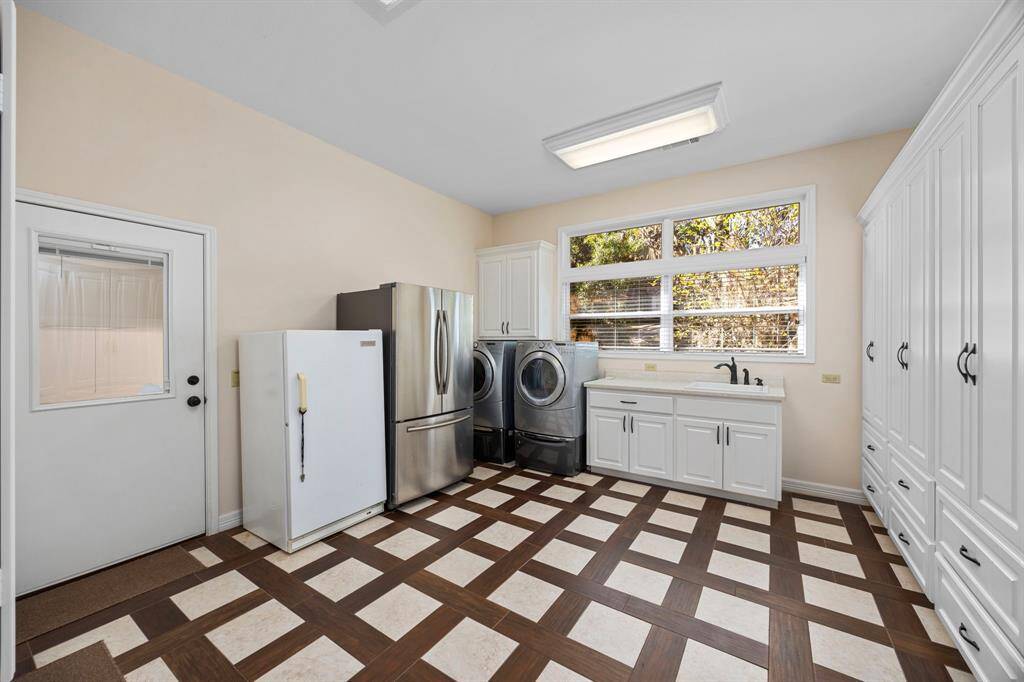The spacious utility room, just off the kitchen, offers ample room for a washer and dryer, an additional refrigerator and freezer, along with plenty of cabinet and drawer space for organized storage.  Note - door on left side of photo leads into the 3-car garage.