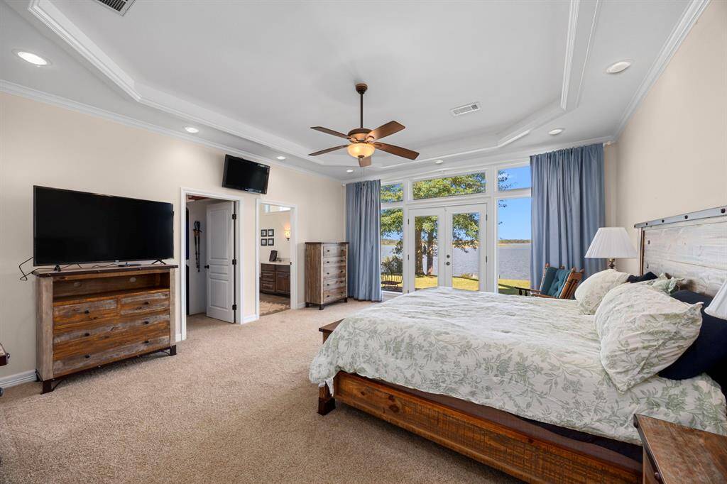 Primary bedroom with Walk-in closet through opening on left, and full en-suite bathroom through opening on right.  French doors and windows offer stunning views of waterfront.