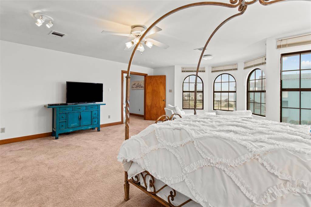 Bright and spacious primary bedroom featuring large arched windows, a cozy carpet, and a stylish ceiling fan. This primary bedroom is located on the second floor with views of the beach.  Natural lighting brings in the daylight hues with while recessed lighting provides optional lighting and dimming choices.