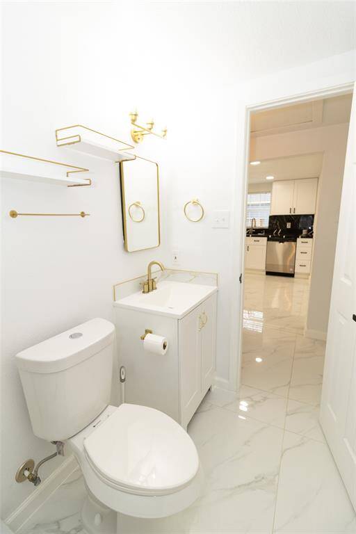 This is a modern and sleek full bathroom featuring white fixtures, marble flooring, and gold accent hardware.