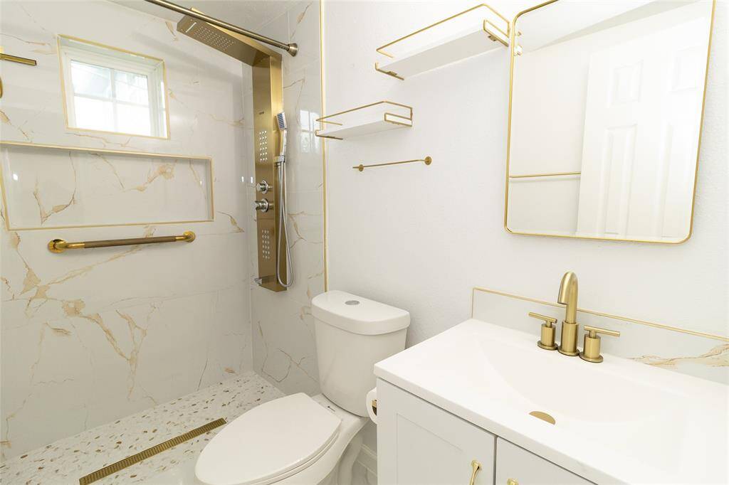 This is a modern and sleek full bathroom featuring white fixtures, marble flooring, and gold accent hardware.