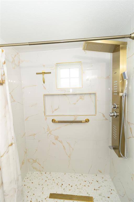 This is a modern and sleek full bathroom featuring white fixtures, marble flooring, and gold accent hardware.