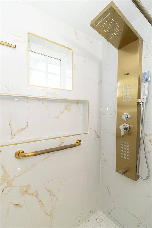 This is a modern and sleek full bathroom featuring white fixtures, marble flooring, and gold accent hardware.