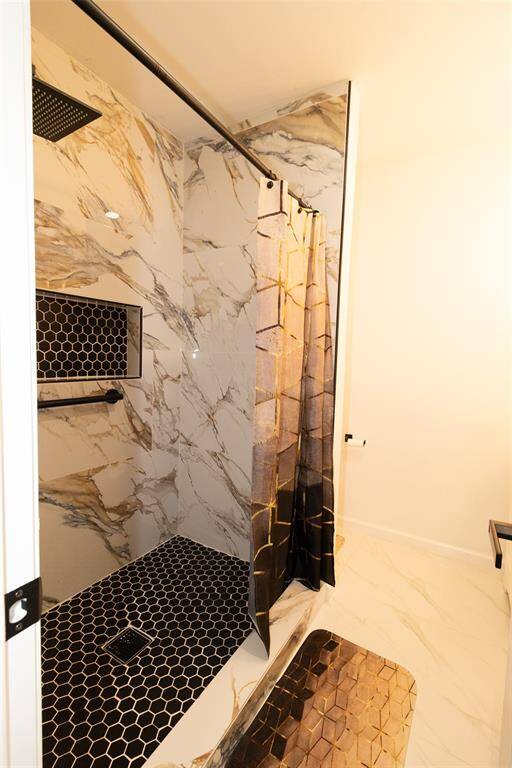 This is a modern walk-in shower with marble walls, featuring a black honeycomb tile floor and  rainfall showerhead.