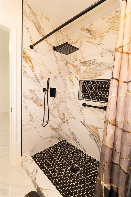 This is a modern walk-in shower with marble walls, featuring a black honeycomb tile floor and  rainfall showerhead.