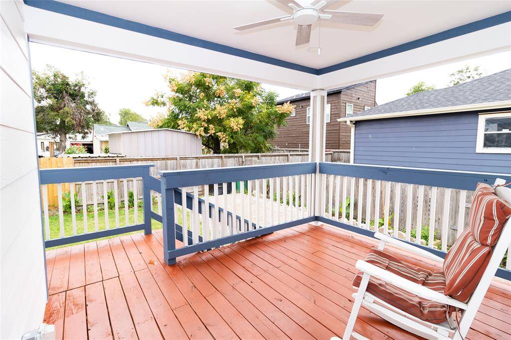 This is a spacious, covered outdoor deck with a fresh wooden floor and a ceiling fan, overlooking a fenced backyard.