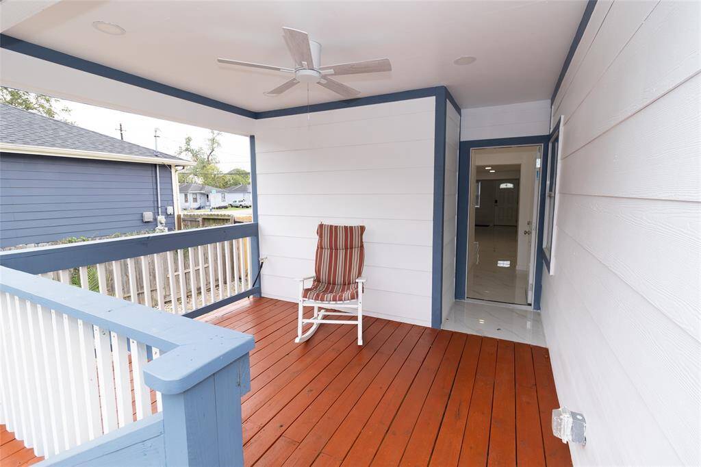 This is a spacious, covered outdoor deck with a fresh wooden floor and a ceiling fan, overlooking a fenced backyard.
