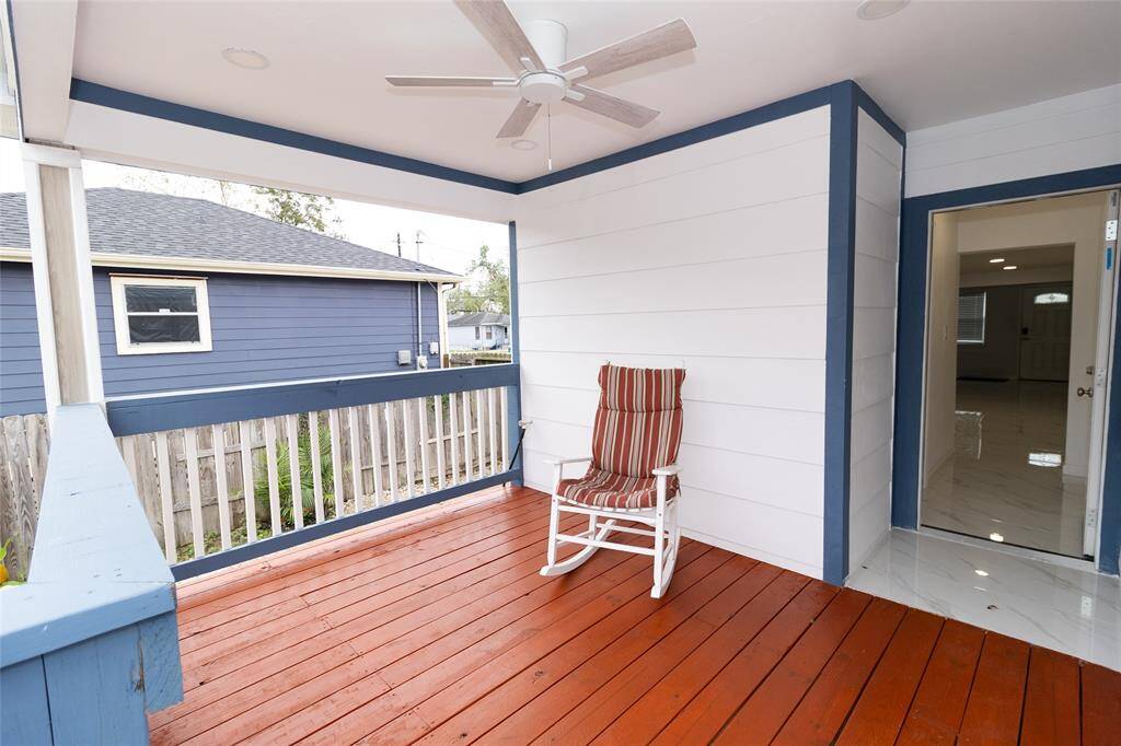 This is a spacious, covered outdoor deck with a fresh wooden floor and a ceiling fan, overlooking a fenced backyard.