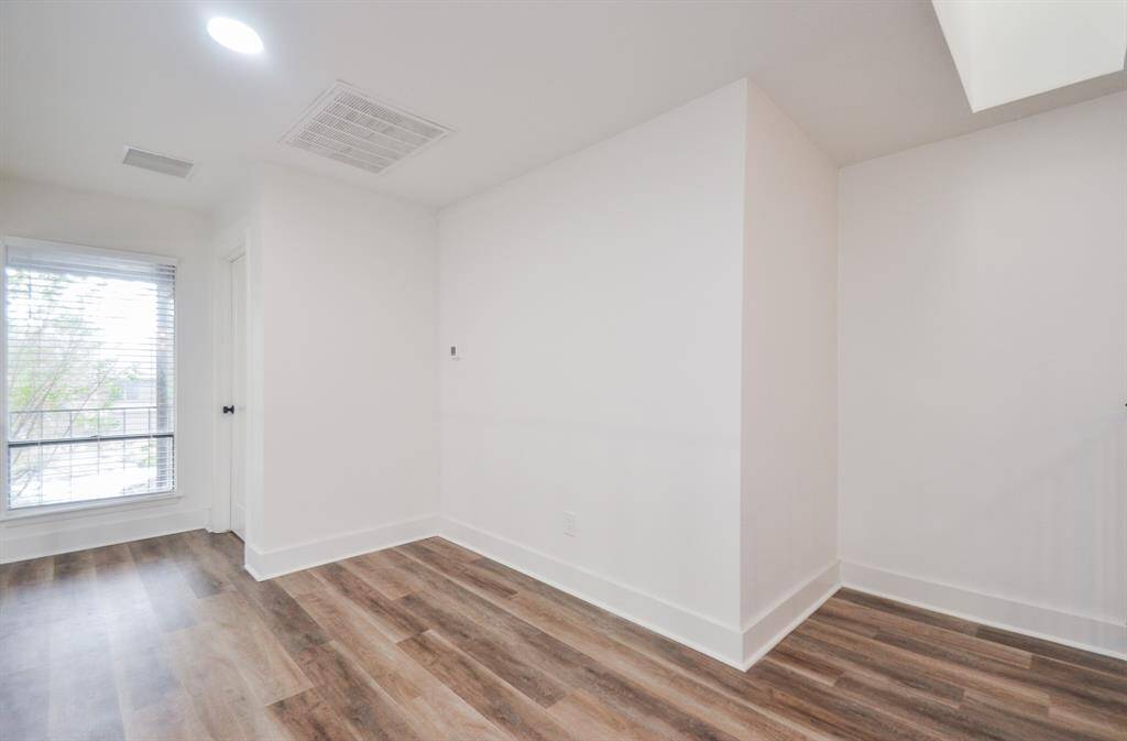 This is a bright, modern room featuring fresh white walls, wood-look flooring, and a large window allowing for natural light. It has a clean, minimalist design with ample wall space for customization.
