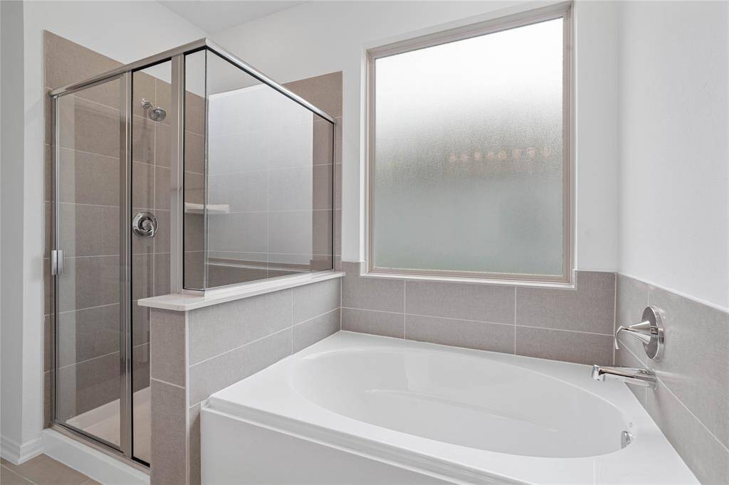 Another view of the primary bathroom featuring dark framed walk-in shower with tile surround and separate garden tub for soaking after a long day with custom tile detailing.