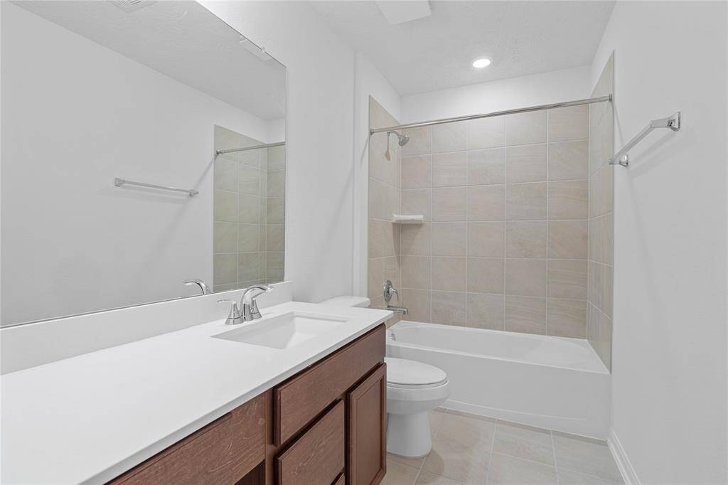 Secondary bath features tile flooring, bath/shower combo with tile surround, stained wood cabinets, beautiful light countertops, mirror, sleek fixtures and modern finishes.