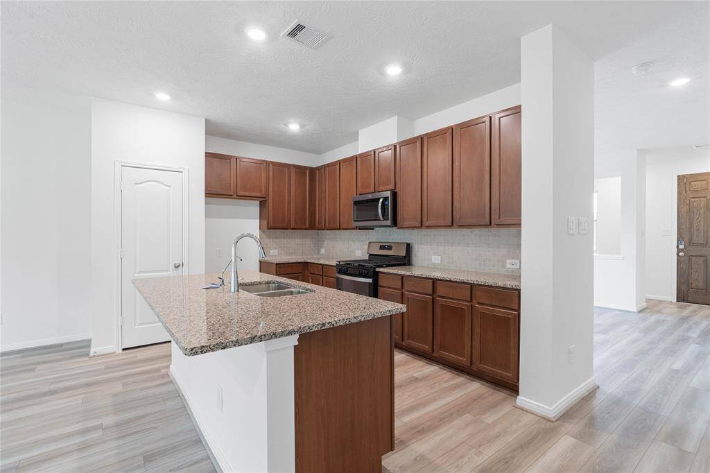 This spacious kitchen features high ceilings, stained wood cabinets, granite countertops, SS appliances including microwave, modern tile backsplash, recessed lighting, huge granite kitchen island extended for a breakfast bar, and a pantry all overlooking your huge family room.