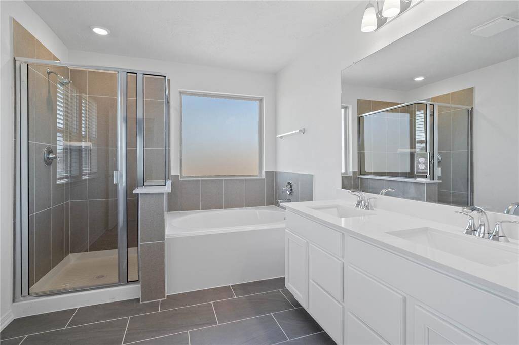 This primary bathroom is definitely move-in ready! Featuring a walk-in shower and separate garden tub with tile surround, stained cabinets with light countertops, dual vanities, high ceilings, large window, neutral paint, sleek and modern finishes.