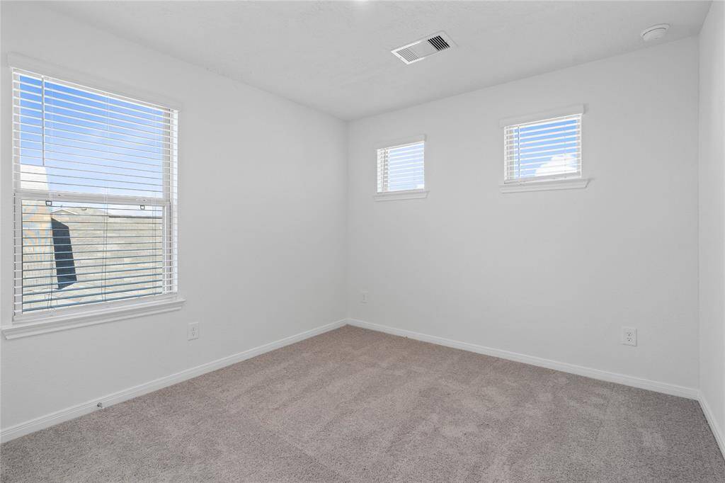 Secondary bedroom features plush carpet, neutral paint, lighting, large windows with blinds, and ample sized closet space.