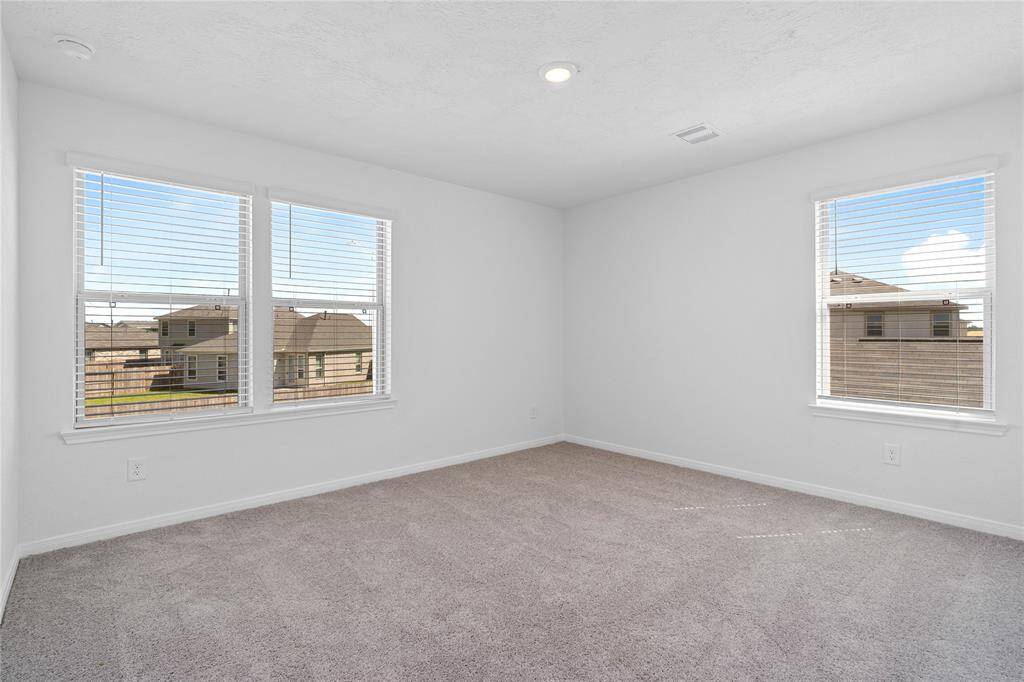 Secondary bedroom features plush carpet, neutral paint, lighting, large windows with blinds, and ample sized closet space.