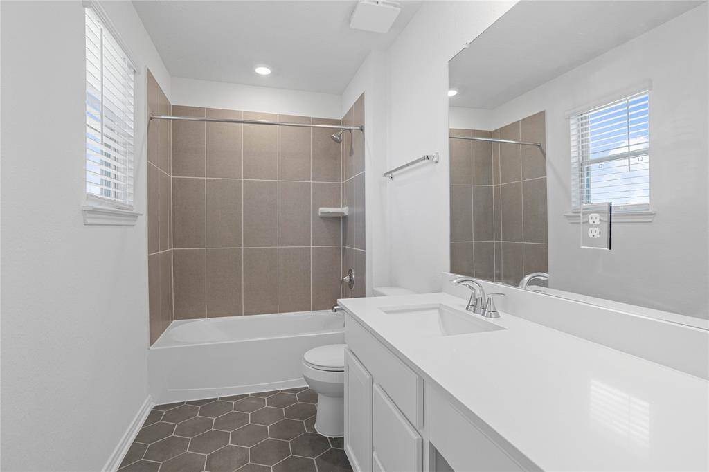 Secondary bath features tile flooring, bath/shower combo with tile surround, stained wood cabinets, beautiful light countertops, mirror, sleek fixtures and modern finishes.
