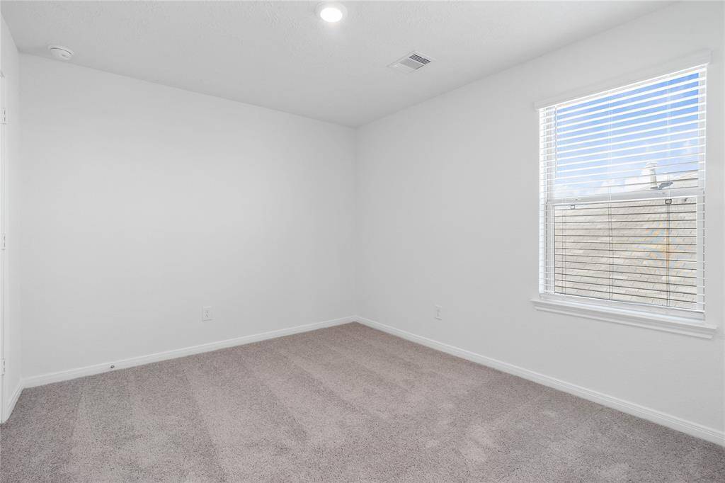 Secondary bedroom features plush carpet, neutral paint, lighting, large window with blinds, and ample sized closet space.