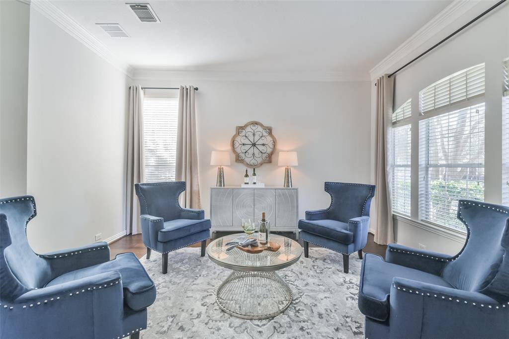 The formal living room has wood floors, double crown molding, a curved window with 2” blinds, custom drapes, and columns.