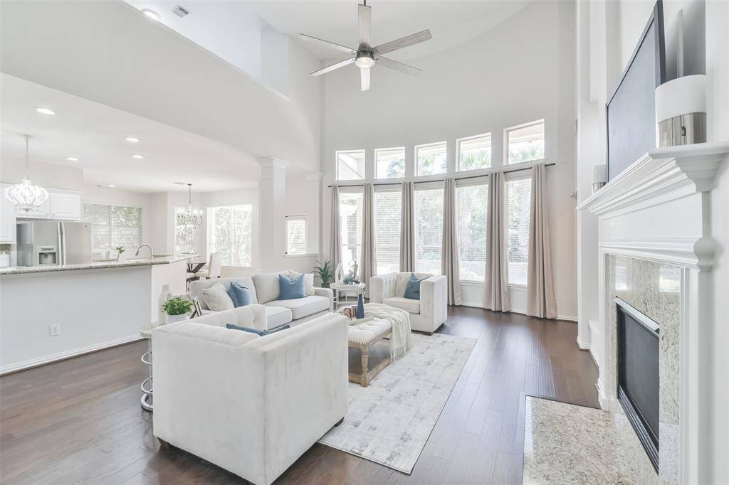 The family room has wood floors, soaring ceilings, a ceiling fan, and a wall of windows with 2” blinds and custom drapes.