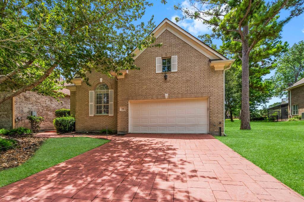 This is a two-story brick home featuring a two-car garage, arched windows, and a well-maintained lawn, nestled among mature trees in a suburban setting.