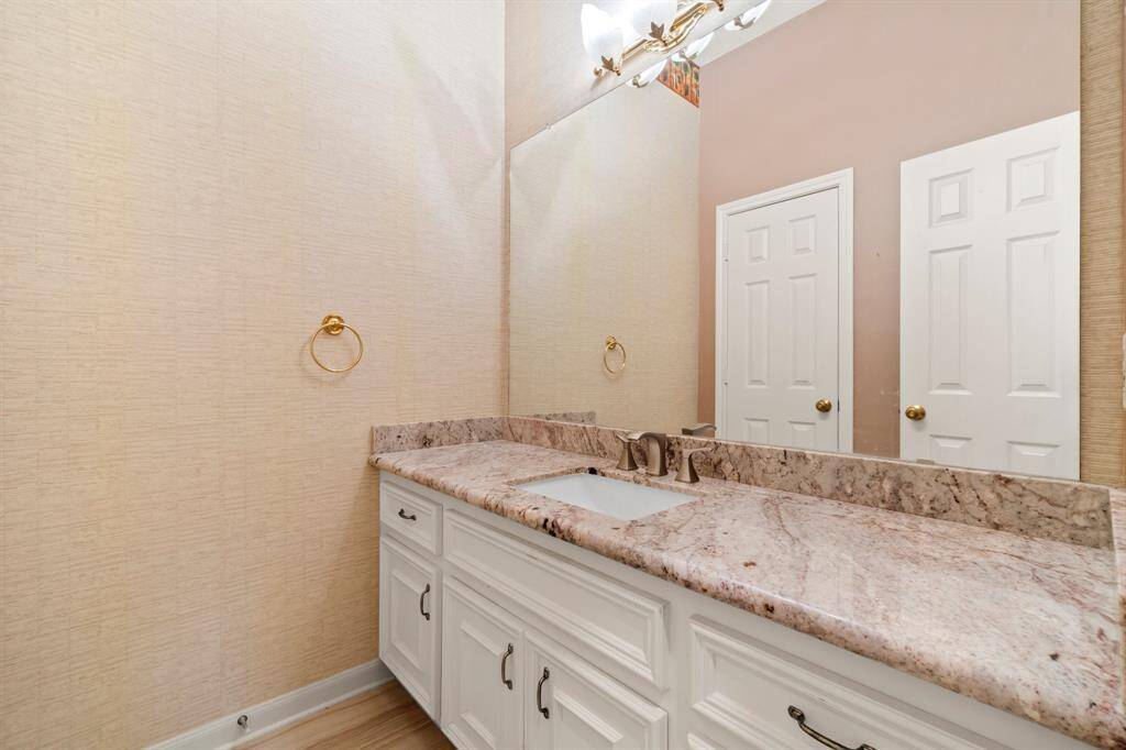 This is a well-maintained bathroom featuring a large vanity with marble countertop, undermount sink, and ample cabinet space. There's also a large mirror and tasteful gold-toned fixtures.