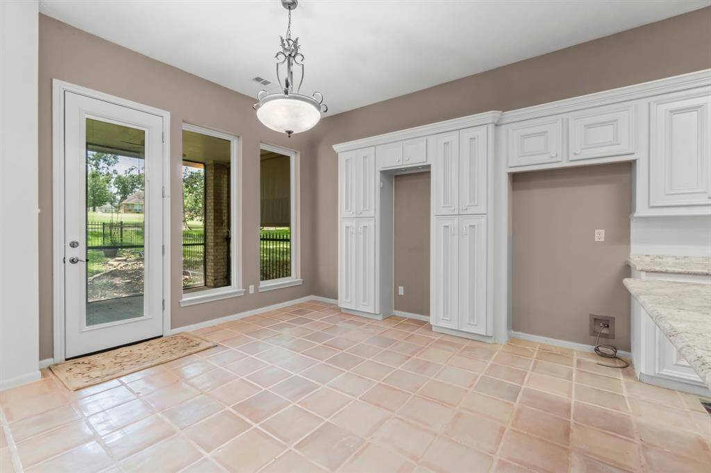 This is a spacious room featuring tiled flooring, large windows with a view of the backyard, French doors leading outside, and built-in cabinetry. The room has plenty of natural light and appears to be in a serene location.