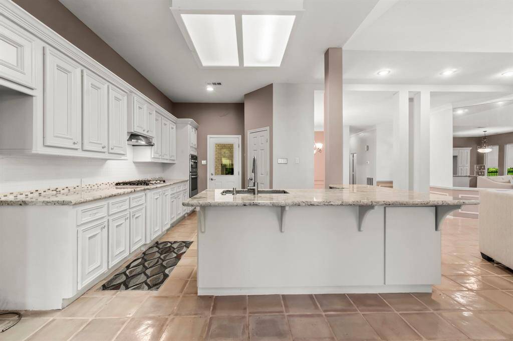 This is a spacious kitchen featuring white cabinetry, granite countertops, and a central island. It opens up to the adjoining living areas, creating a flowing, open-plan space, enhanced by natural light from skylights.
