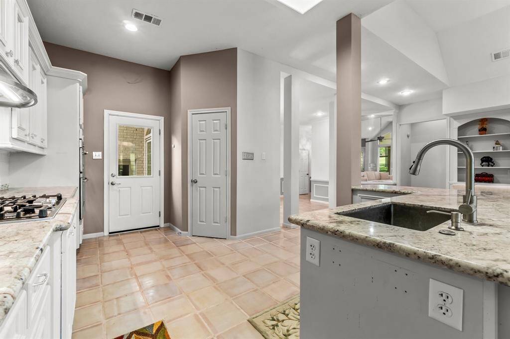 This is a spacious, well-lit kitchen featuring white cabinetry, granite countertops, and modern stainless-steel appliances, with a view into an adjoining room and a door leading outside.