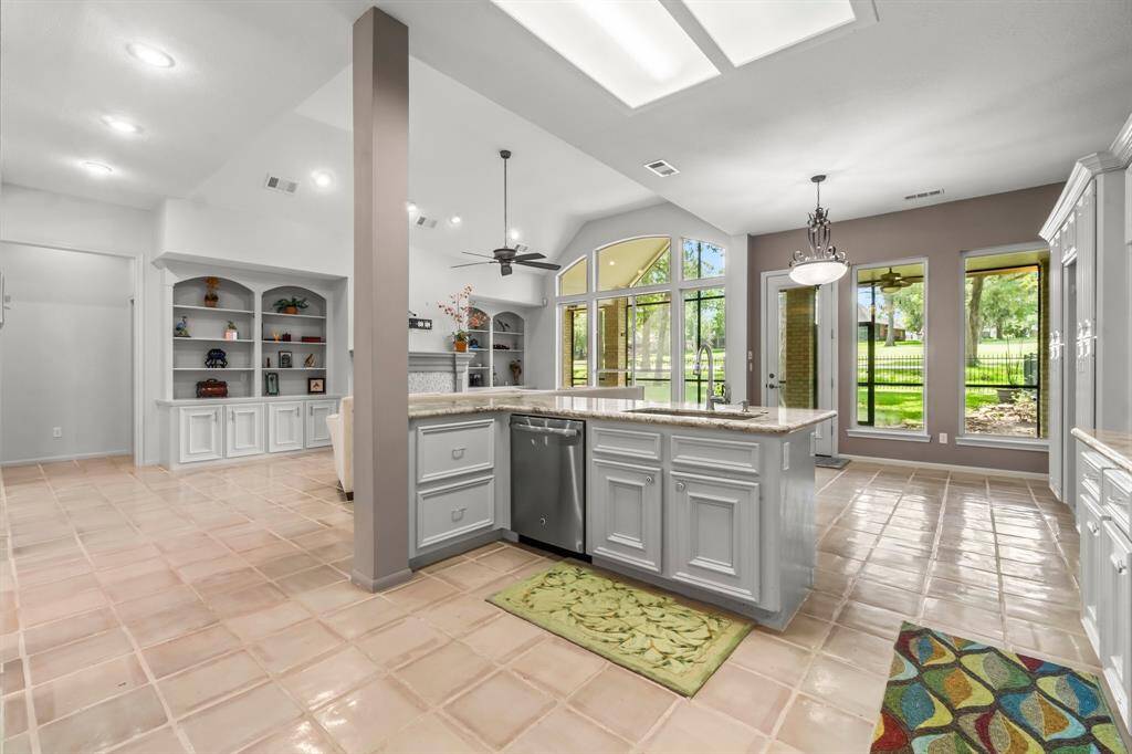 This is a spacious, well-lit kitchen with modern appliances, a large island, ample cabinetry, and a view of the yard through large windows. There's also a built-in shelving unit for extra storage or display.