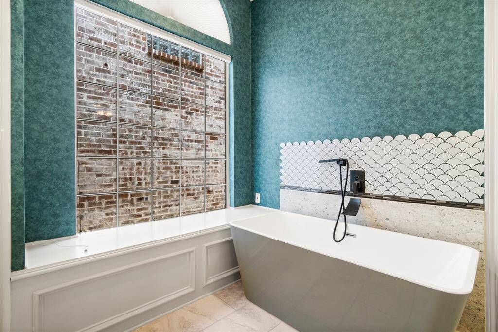 You're looking at a modern bathroom featuring an elegant freestanding bathtub with a sleek black faucet, set against a backdrop of stylish fish scale tiling and a large window with privacy glass. The room is accented with a rich teal wallpaper, providing a contemporary and serene space.