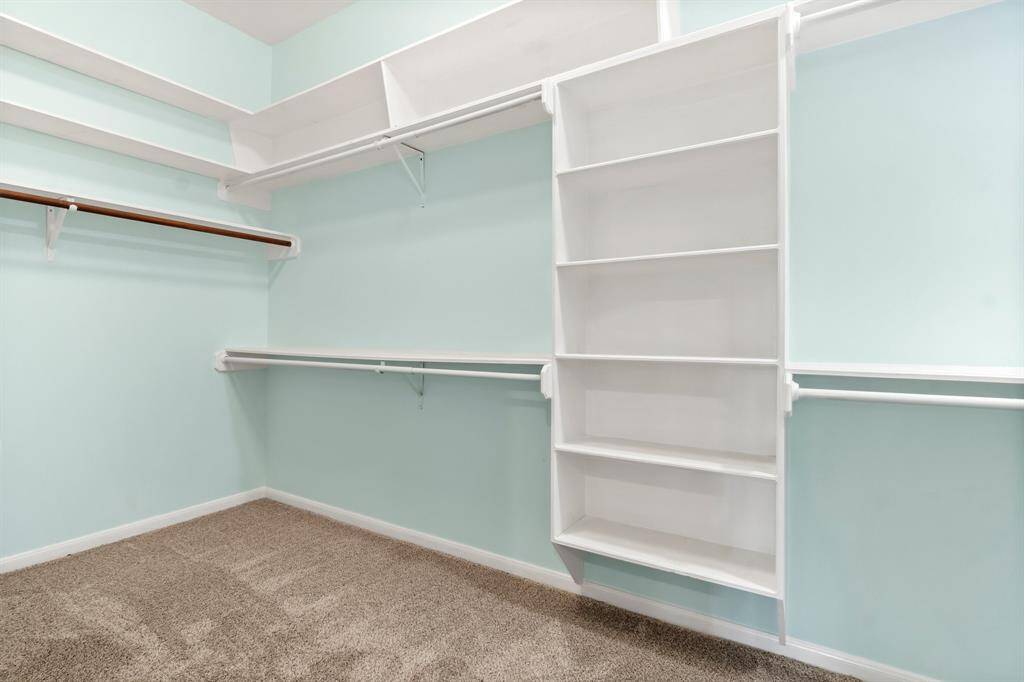 This is a spacious walk-in closet featuring built-in shelves and hanging rods, with a light blue color scheme and carpeted flooring.