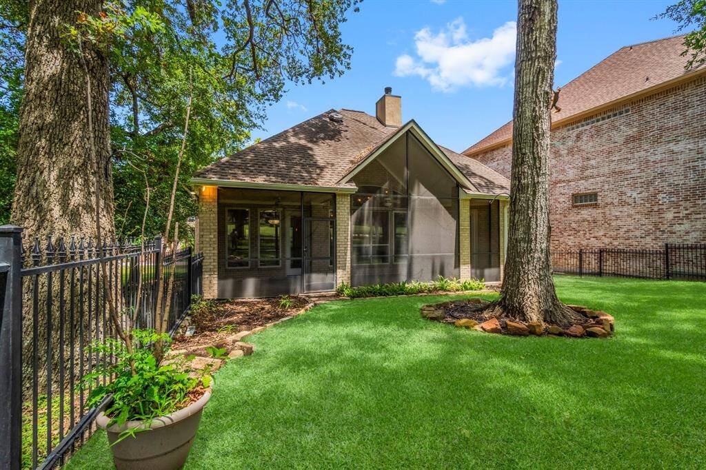 This is a single-story home featuring a brick exterior, a well-maintained lawn, mature trees, and a screened-in porch area, enclosed by a wrought-iron fence.