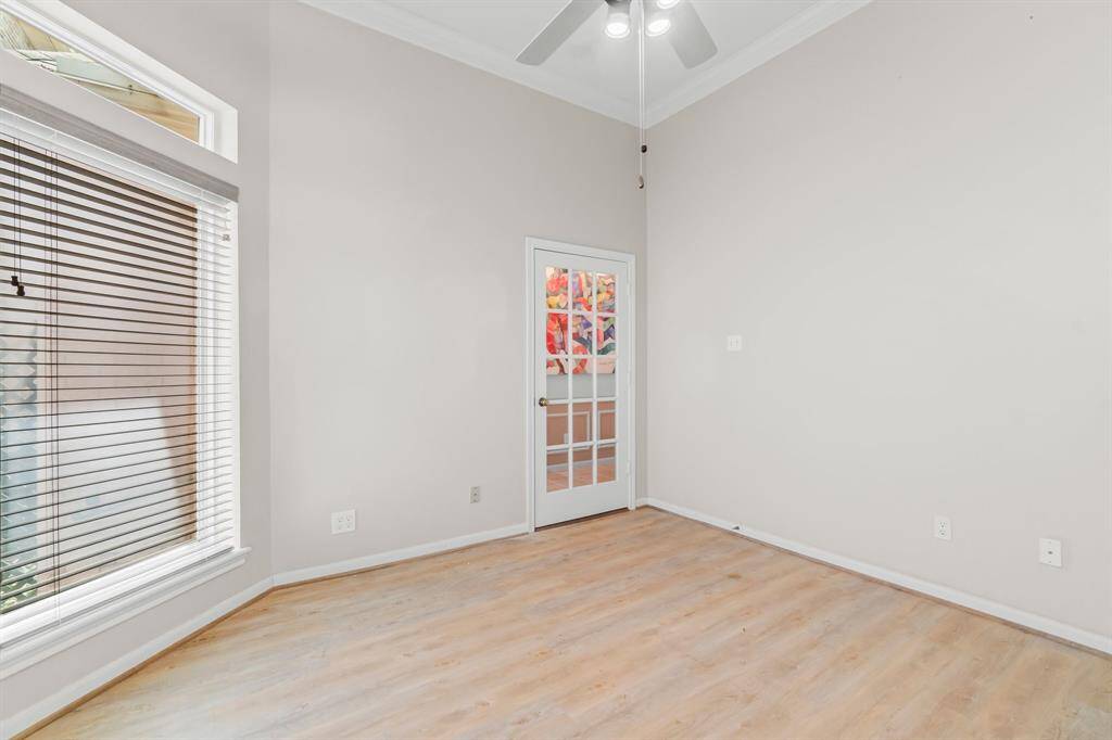 The room features neutral-colored walls, a vaulted ceiling with a skylight, light hardwood flooring, a large window with horizontal blinds, and a glass-paned door leading to another room.