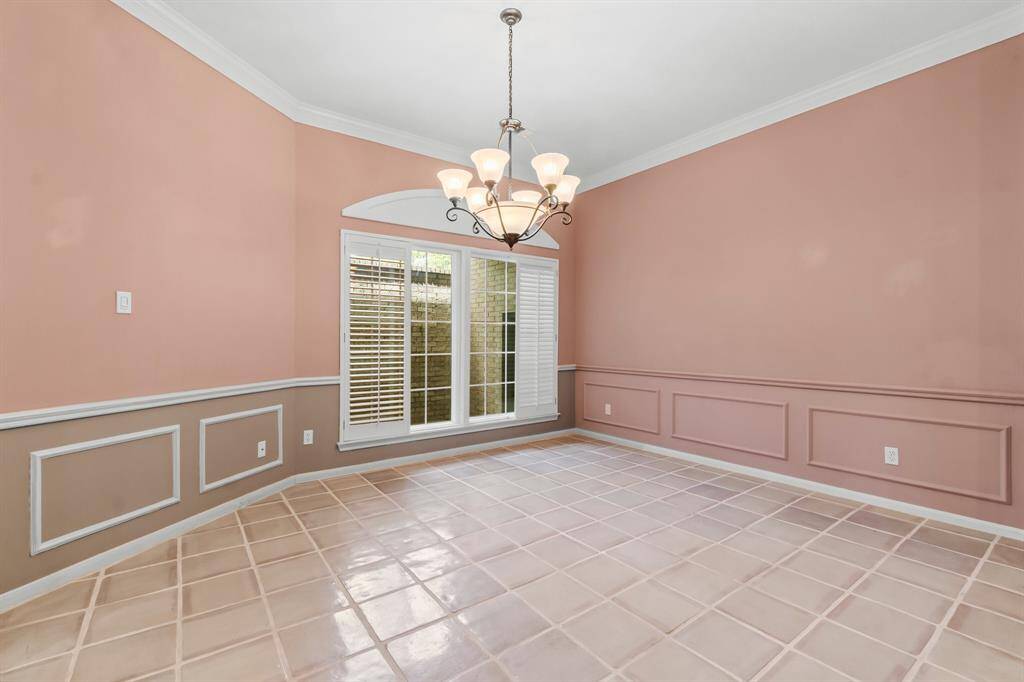 This is a spacious room featuring salmon-colored walls with white chair railing and wainscoting, a tiled floor, and an arched window providing natural light. The room is finished with a classic chandelier.