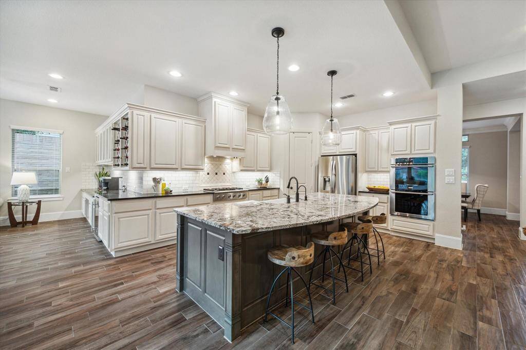 A chef's dream kitchen equipped with oversized island, upgraded granite countertops, double oven, 6 burner gas range stove, stainless steel appliances, porcelain sink, wine fridge, under cabinet lighting and tons of storage!