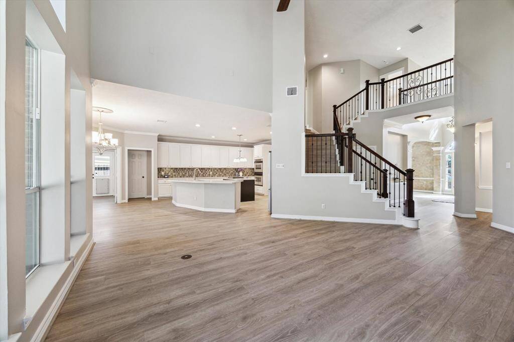 Elegant entryway featuring a wooden and wrought- iron staircase with decorative iron spindles, leading to a bright, open-concept interior with warm wood floors and refined finishes.