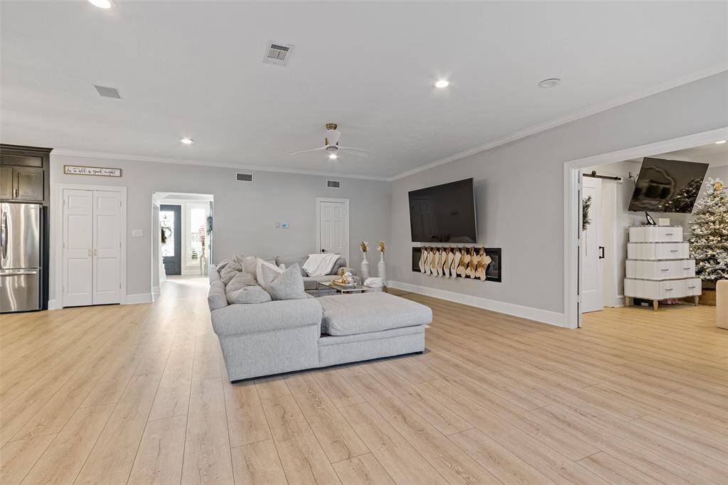 Spacious and modern living room with engineered wood flooring. It features a cozy fireplace, recessed lighting, and an open layout that leads to adjacent rooms, creating a welcoming and versatile space.