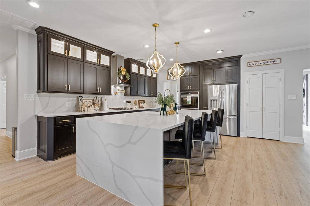Another view of this beautiful kitchen with quartz counters, stainless steel appliances, and plenty of light. Cabinets have been painted a tan color recently.