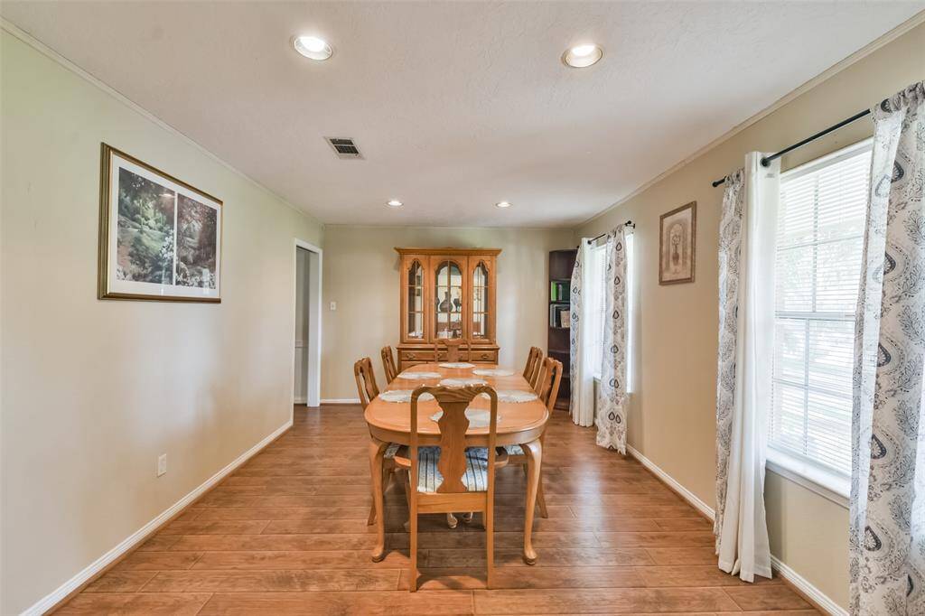 Elegant dining room featuring wood-look flooring, a large dining table, and a classic china cabinet. Natural light streams through the windows adorned with patterned curtains, creating a warm and inviting atmosphere for gatherings