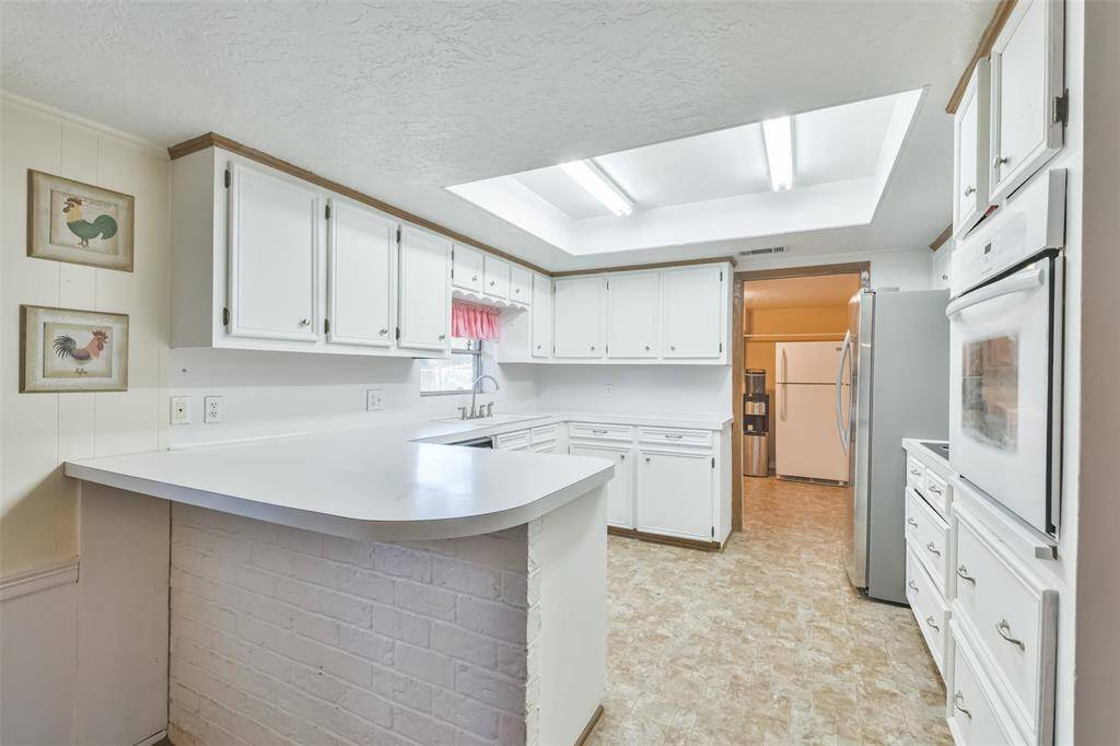 Bright kitchen featuring crisp white cabinetry, ample counter space, and a charming breakfast bar with a brick accent. The appliances add modern functionality