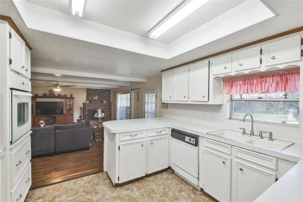Bright kitchen with a convenient open layout connecting to the living room, featuring white cabinetry, ample counter space, and a charming window above the sink. The breakfast bar provides a perfect space for casual dining.