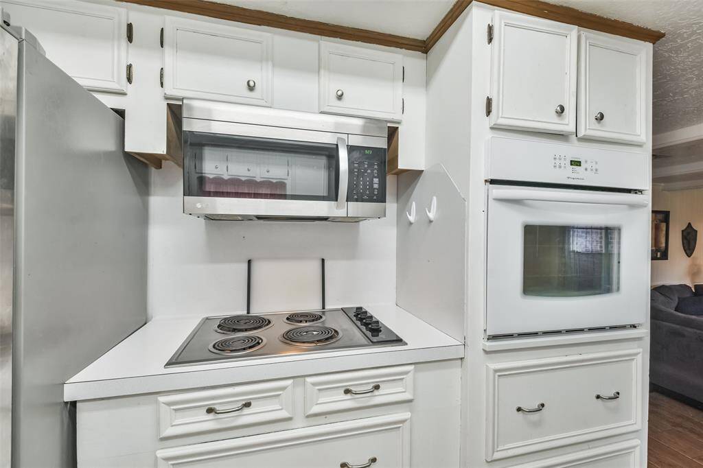 Compact cooking area equipped with a stainless steel microwave, built-in oven, and electric cooktop. White cabinetry provides a clean, cohesive look with ample storage for kitchen essentials