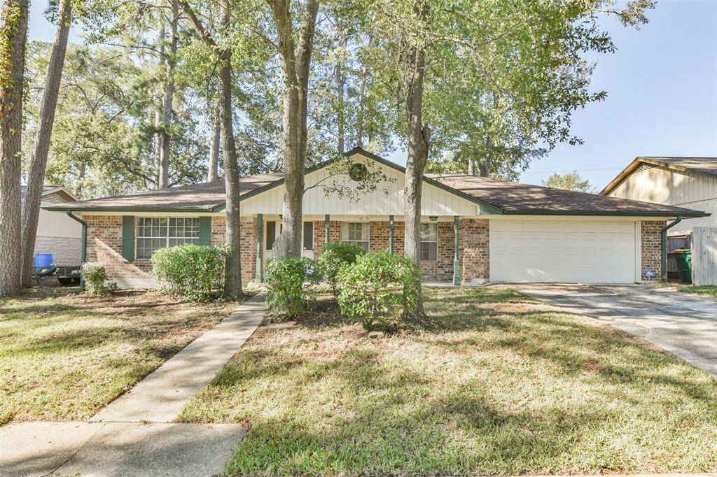 This inviting brick home features a classic facade, a covered porch, and a two-car garage, set amidst a beautifully shaded lot with mature trees and manicured landscaping